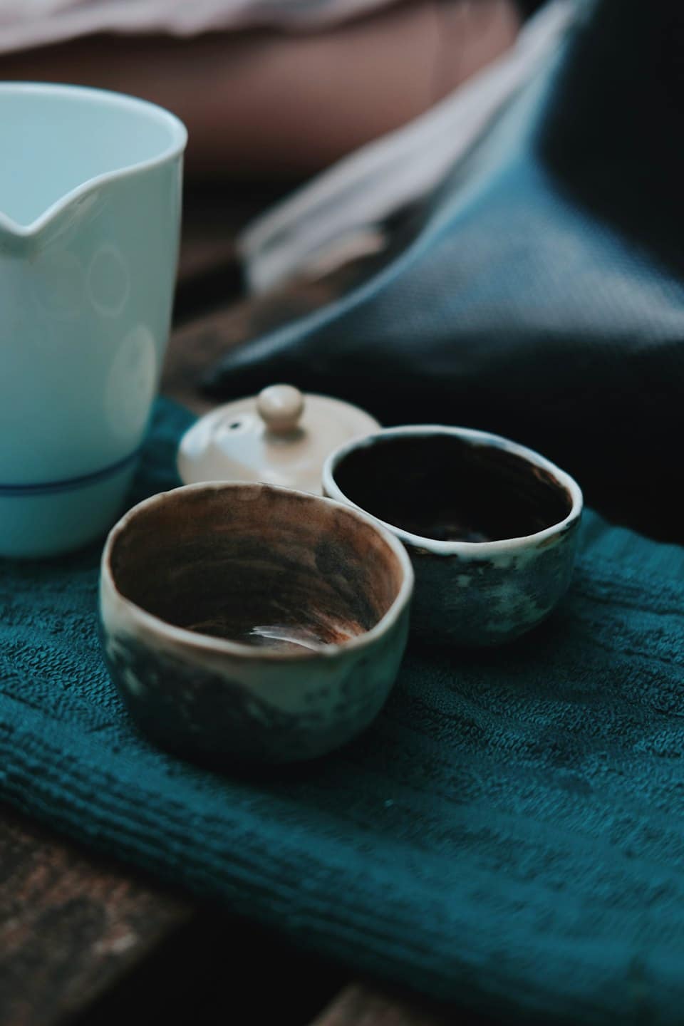 Ceramic teacups and a teapot lid rest on a cloth.